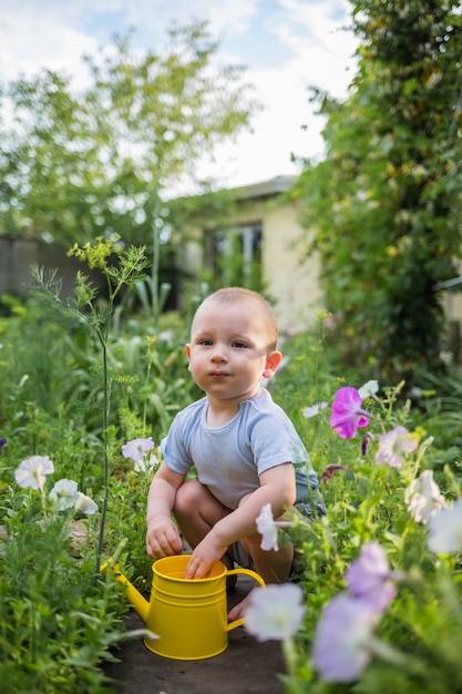 A little helper boy is sitting in the garden with a yellow watering can