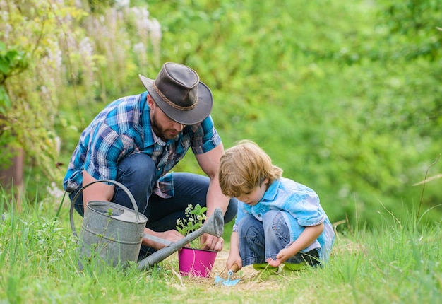 Little helper in garden Make planet greener Growing plants Take care of plants Day of earth Boy and father in nature Gardening tools Planting flowers Dad teaching little son care plants