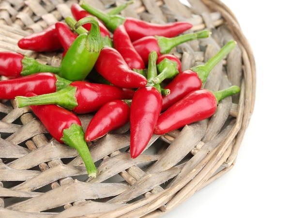 Little hot peppers on wicker mat isolated on white