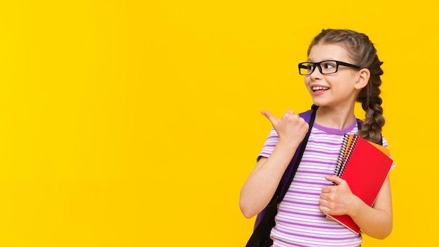 A little joyful girl holds notebooks in her hand and points to the side at your advertisement