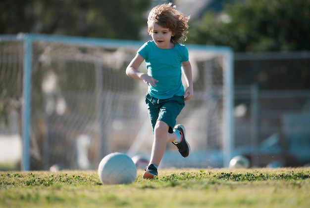 Little kid boy running and playing football in the field with soccer ball concept of children sport