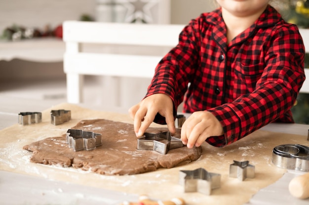 little kid girl in red pajama cooking festive gingerbread in christmas decorated kitchen