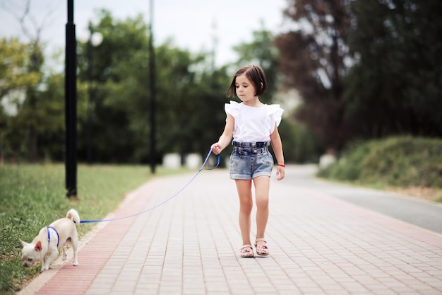 Little kid girl walking in park with pet puppy outdoors