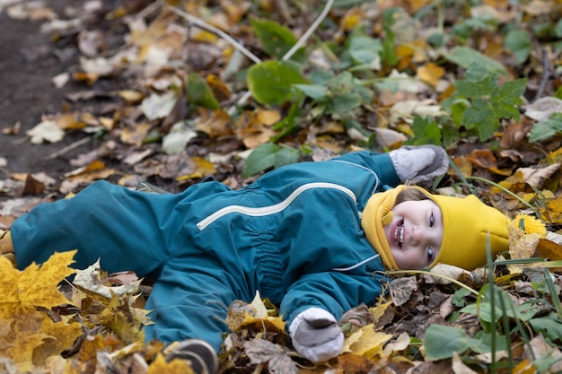 Little kid lying in autumn leaves having fun in forest