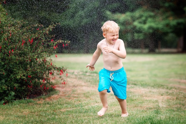 Little kid playing with water on hot summer day Boy with garden sprinkler Boy runs on a field under water drops