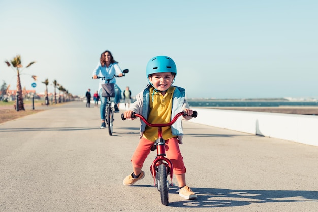 Little kid riding a balance bike with his mother on a bicycle in a city park