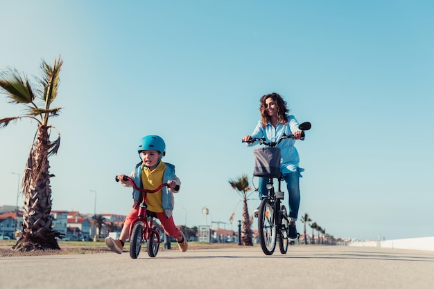 Little kid riding a balance bike with his mother on a bicycle in a city park