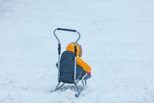 Little kid at sledge sliding down by winter hill