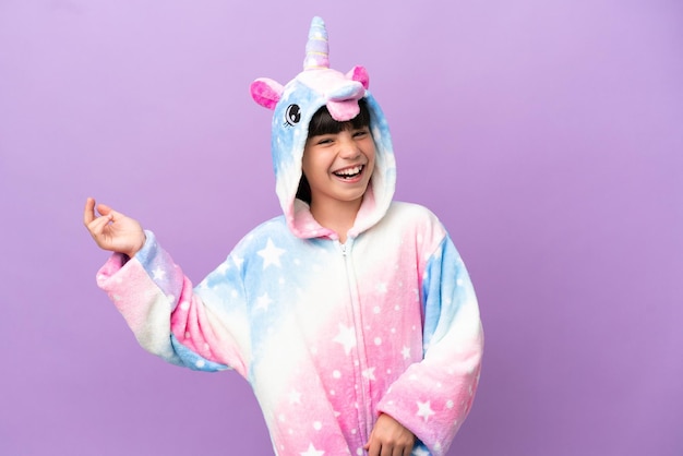 Little kid wearing a unicorn pajama isolated on purple background making guitar gesture