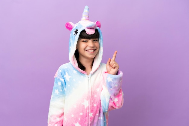 Little kid wearing a unicorn pajama isolated on purple background pointing with the index finger a great idea