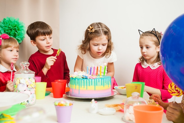 Little kids celebrating birthday. The girl makes a wish before blowing candles on the cake