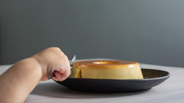 Little kids hand eating pudding desset with metallic spoon on a dark dish over table