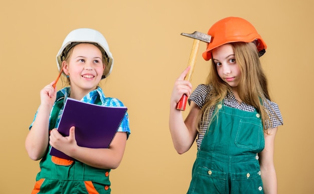 Little kids in helmet with tablet and hammer happy children Future career Foreman inspector Repair Labor day 1 may small girls repairing together in workshop hammer tool work with hammer