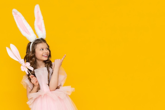 The little lady is celebrating Easter A beautiful little girl with curly hair is enjoying the spring holiday A child with rabbit ears on his head on a yellow isolated background Copy space