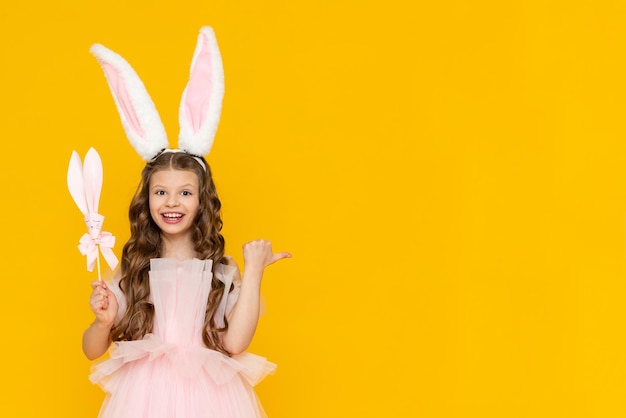 The little lady is celebrating Easter A beautiful little girl with curly hair is enjoying the spring holiday A child with rabbit ears on his head on a yellow isolated background Copy space