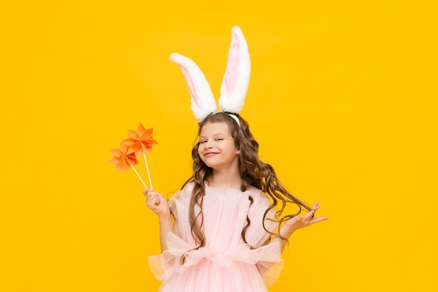 The little lady is celebrating Easter A beautiful little girl with curly hair is enjoying the spring holiday A child with rabbit ears on his head on a yellow isolated background