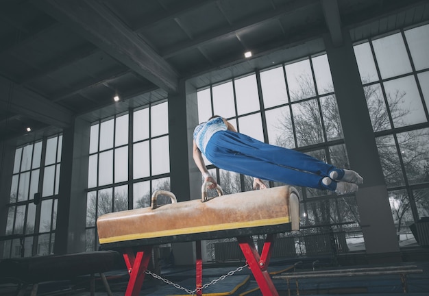 Little male gymnast training in gym, composed and active. Caucasian fit little boy, athlete in sportswear practicing in exercises for strength, balance. Movement, action, motion, dynamic concept