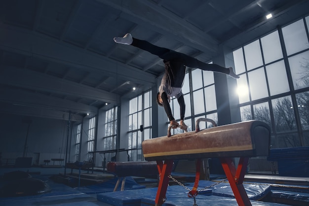 Little male gymnast training in gym, flexible and active. Caucasian fit little boy, athlete in sportswear practicing in exercises for strength, balance. Movement, action, motion, dynamic concept.