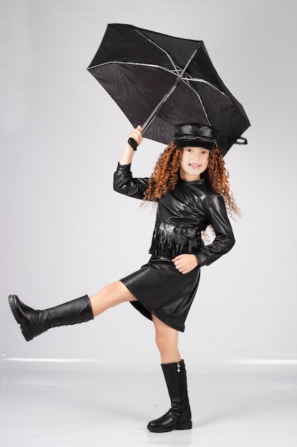 Little model wearing a black dress, holding a black umbrella and raising her leg