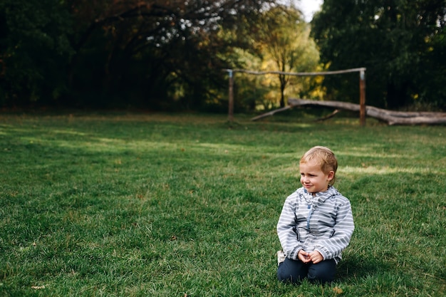 Little naughty boy smile and sit at green meadow, active happy childhood outdoors