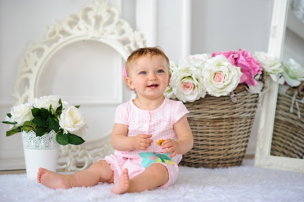 The little one-year-old girl smiles and sits.