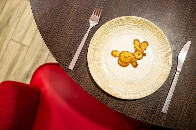 Little pancake in the form of a bunny on a plate next to a knife and fork on a table in a cafe