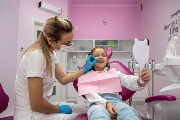 Little patient admires her healthy teeth in the reflected mirrors dentistry examination of children's teeth