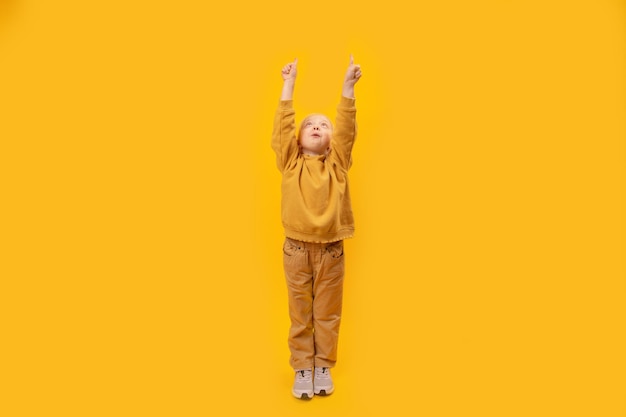 Little preschool girl raised hands up and points index fingers up Child in yellow clothes Copy space