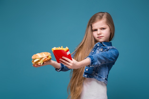 Little pretty girl in jean jacket with long brown hair hold a burger and fried potato