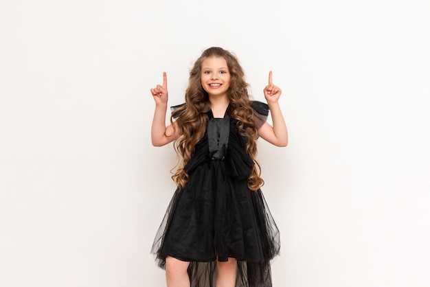 A little princess in a black dress points up with her finger at your advertisement on a white isolated background