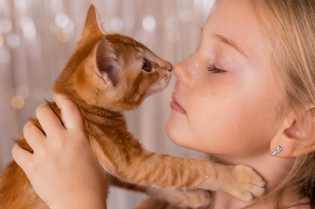 A little princess girl in an elegant dress holds a red kitten in her hands. The symbol of the year