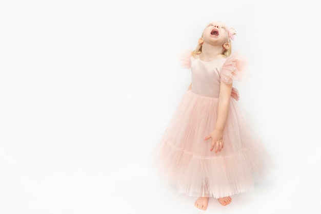 Little princess laughs with head thrown back Cute girl in elegant lush dress and bare feet isolated on white background