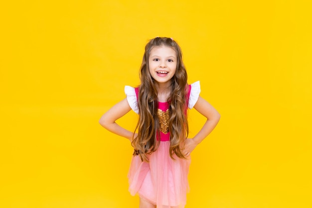 A little princess in a pink dress with curly hair is smiling broadly A beautiful charming child on a yellow isolated background