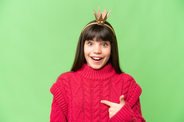 Little princess with crown over isolated chroma key background with surprise facial expression