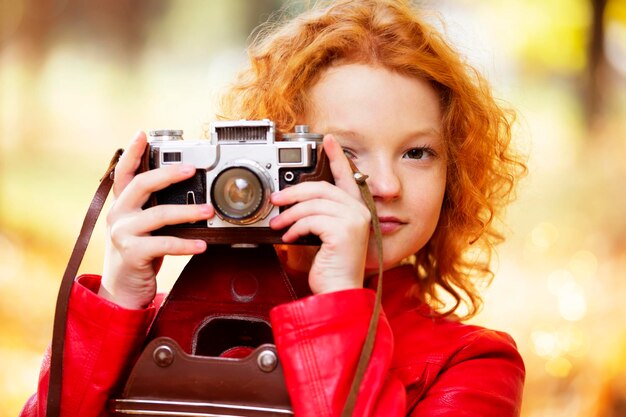 Little redhaired girl with a retro camera on an autumn background