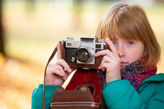 Little redhaired girl with a retro camera in the autumn park Child photographer