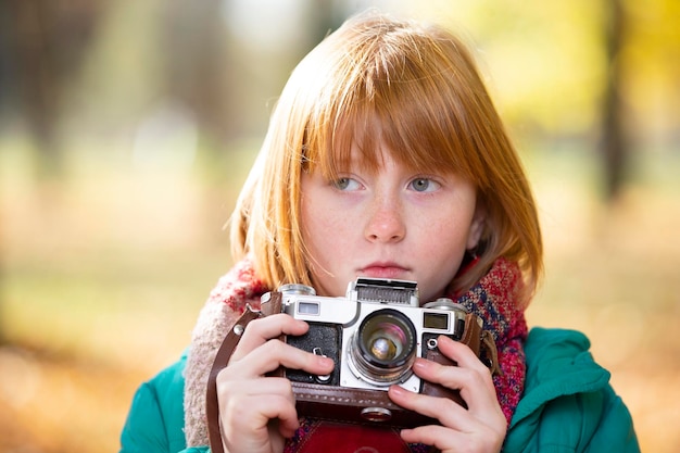 Little redhaired girl with a retro camera in the autumn park Child photographer