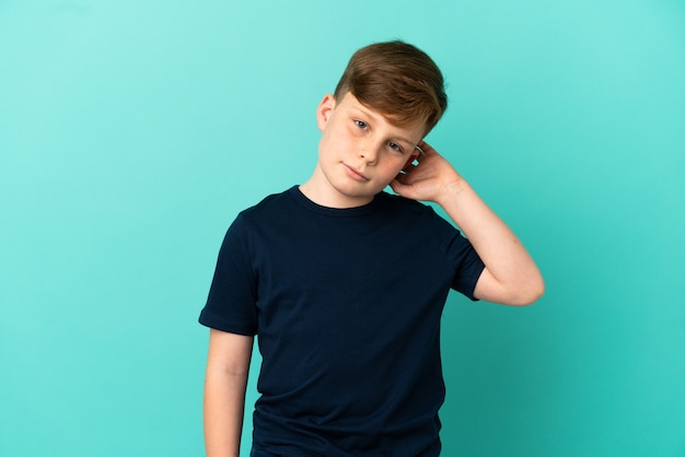 Little redhead boy isolated on blue background having doubts