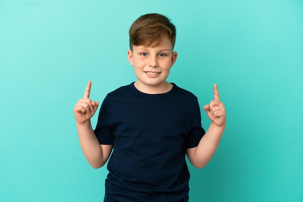 Little redhead boy isolated on blue background pointing up a great idea