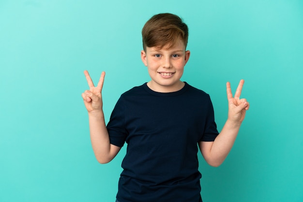 Little redhead boy isolated on blue background showing victory sign with both hands