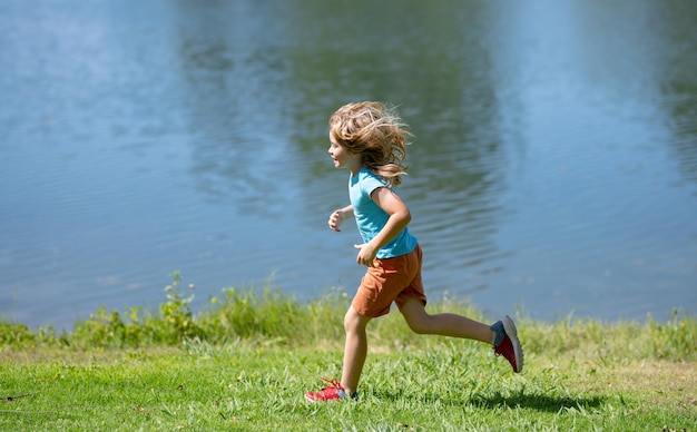 Little runners outdoors in summer nature Sporty child running in a park Outdoor sports and fitness for children Kid boy running on green grass near lake in summer park