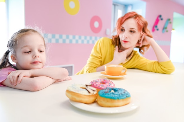 Little sad girl watching on a sweet donuts in a cafe. Diet concept