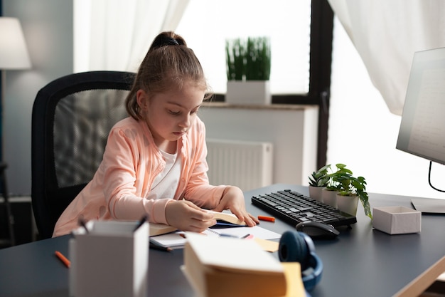 Little schoolgirl taking notes and writing at home desk