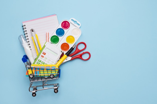 Little shopping cart filled with school stationery on blue table