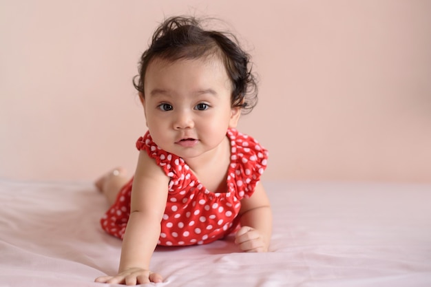 little smiling asian baby dressed in red practicing crawling on the bed with pastel background