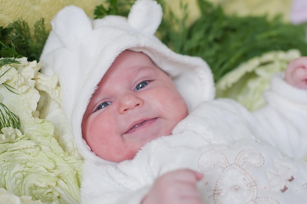 Little smiling baby lays on cabbage leaves