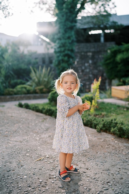 Little smiling girl stands on a path in a sunny park