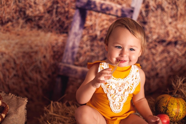 Little smiling girl in the village is sitting in the hay with harvest from vegetables