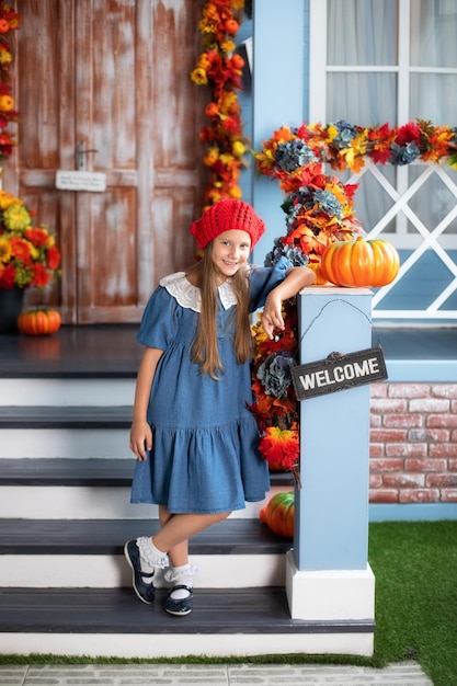 Little smiling happy girl stand with pumpkin on house porch on Halloween.