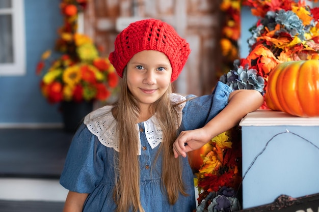 Little smiling happy girl stand with pumpkin on house porch on Halloween.